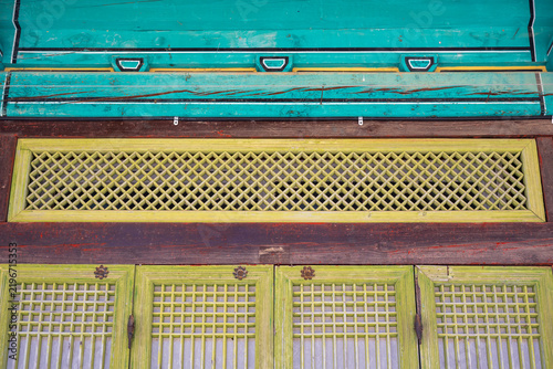 Traditional wooden latticed transom window and doors with painted timber beam on buddhist temple building in South Korea.