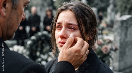 Man wiping tear from crying woman's face at a funeral cemetery, capturing deep grief and emotional support for bereavement counseling and life insurance marketing design.