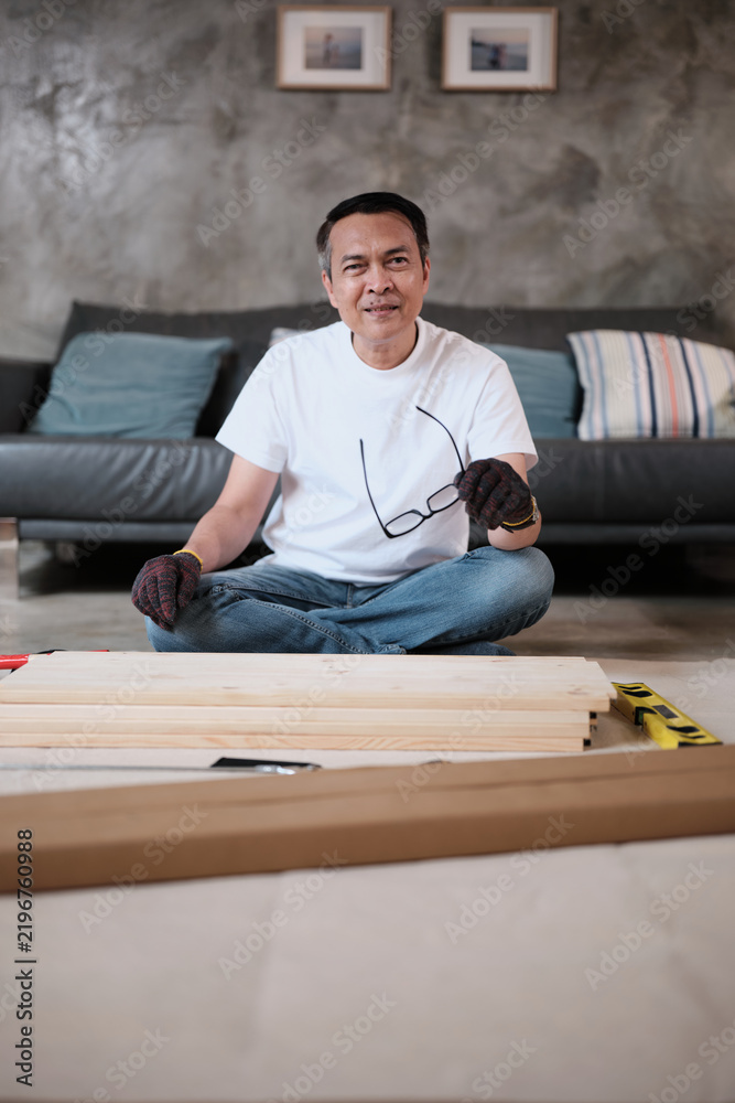 Fototapeta premium Portrait of Asian mature man preparing flat-pack furniture parts, cheerful smile, self-assembly with carpentry diy tools, home improvement, craft install hobby workshop, handyman active lifestyle.