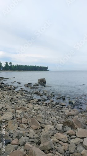 Rocky shoreline of Lake Baikal with distinctive rock formations rising from calm clear water, pebble beach and serene natural landscape under cloudy sky