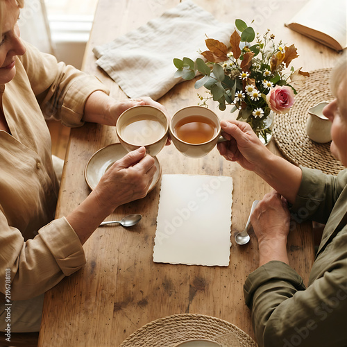 Photorealistic overhead photo of two friends’ hands sharing tea beside a simple handwritten blank card and flowers, warm natural light, cozy neutral table setting, no readable text and no branding.