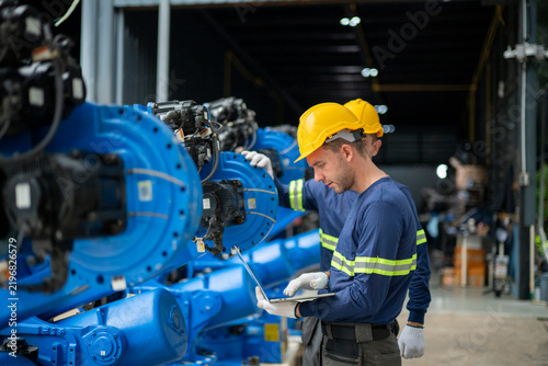 Engineer working on robot arm at factory with laptop