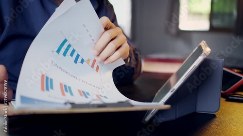 Businessman reviewing and flipping through financial performance report documents on a clipboard at his desk.