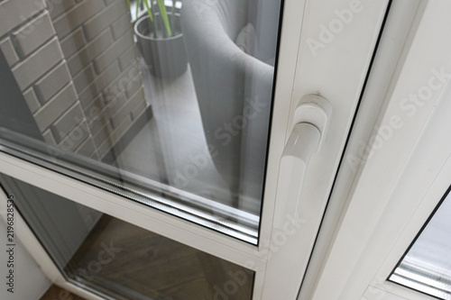 White PVC window frame, double-glazed pane, ergonomic white handle, clean profile lines, subtle shadow, neutral tones, textured brick wall, gray planter, green foliage, modern glazing