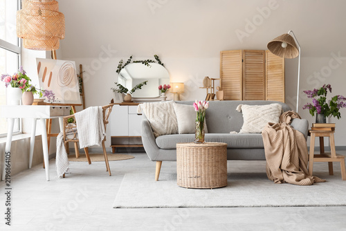 Interior of light living room with sofa, basket and spring flowers in vases