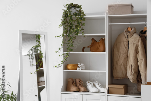 Wardrobe with winter female clothes, accessories and mirror in stylish room