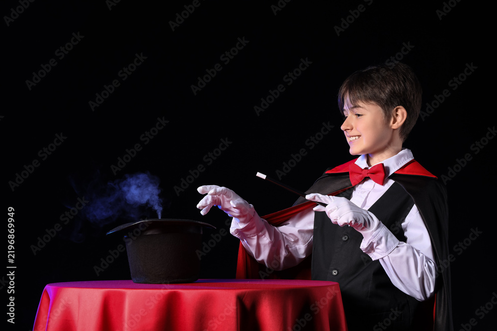 Obraz premium Little magician with wand and hat at table on black background