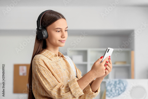 Teenage girl in headphones using mobile phone at home