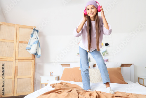 Teenage girl with headphones listening to music in bedroom