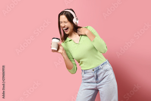 Happy young woman with modern headphones and cup of coffee listening to music...