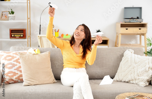 Young Asian woman with paper planes sitting on sofa at home