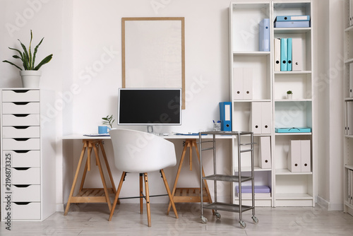 Interior of medical office with doctors workplace and shelf unit