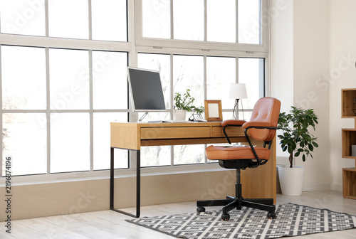 Brown leather swivel chair and workplace with modern computer near window in ...