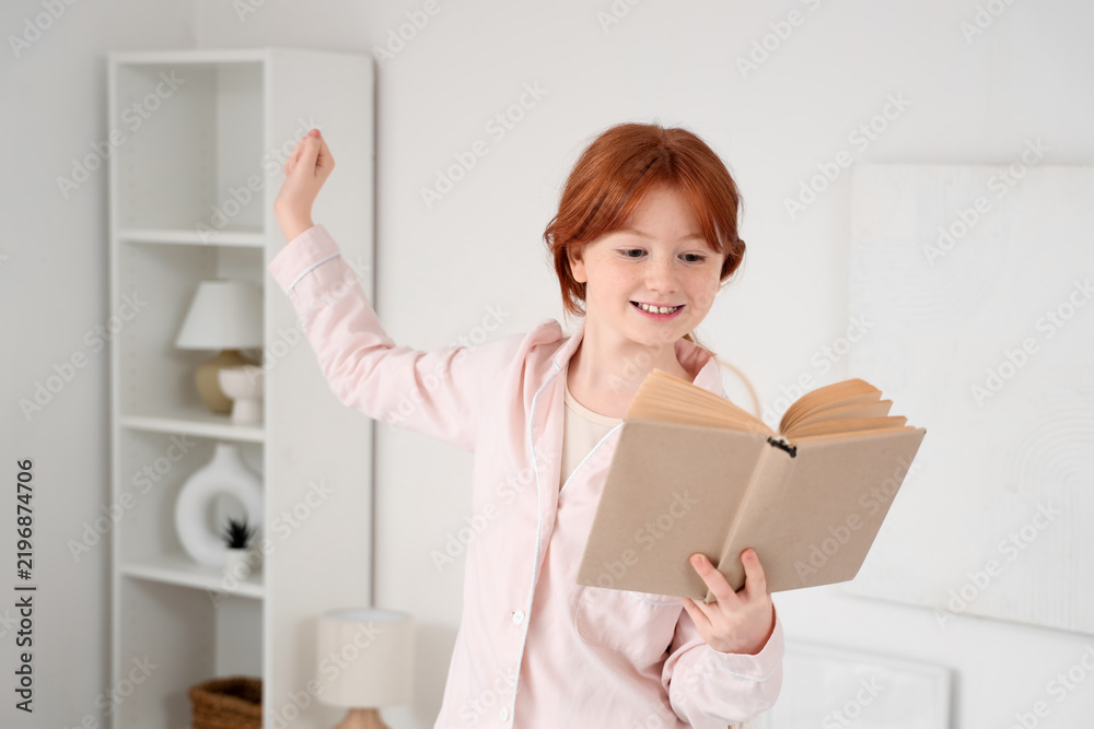 Fototapeta premium Cute teenage happy redhead girl in pajamas reading adventure book at home