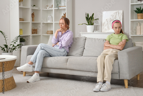 Sad teenage girl sitting on sofa after quarrel with her mother at home. Famil...