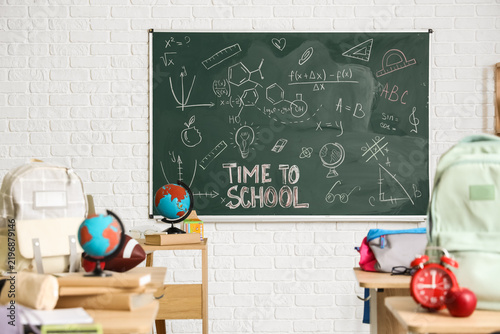 School desks with apple, backpacks, globes and clock in light classroom