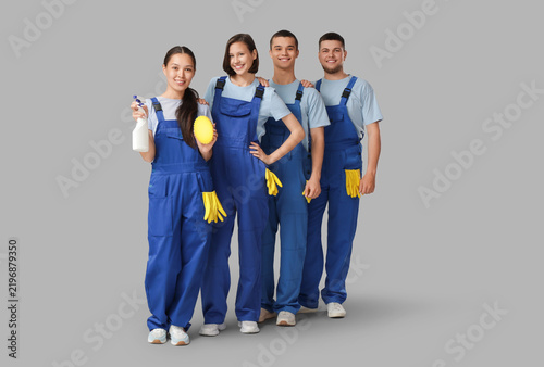 Group of young janitors with cleaning supplies on grey background