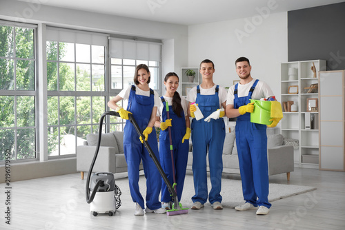 Team of young janitors with cleaning supplies in room