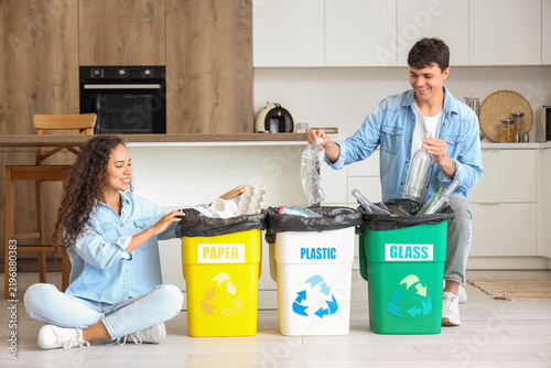 Fotografie Young couple with garbage containers sorting rubbish in kitchen