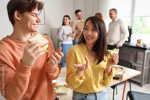 Business people with sandwiches having lunch in office kitchen