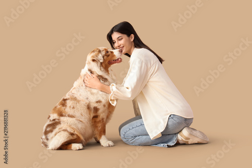 Young woman with Australian Shepherd dog sitting on beige background