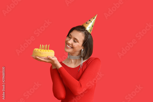 Beautiful woman in party hat with Birthday cake on red background