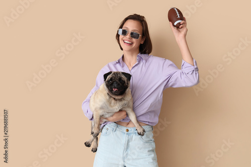 Young woman with cute pug dog and toy ball on beige background