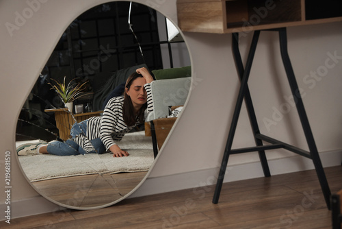 Broken mirror with reflection of depressed young woman at home