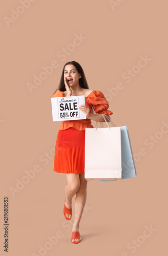Beautiful young shocked woman holding shopping bags and paper with text SUMME...
