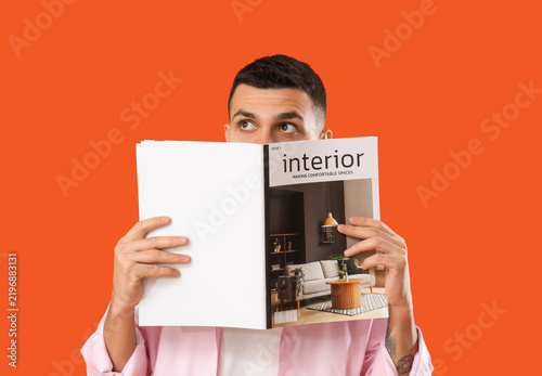 Young man reading magazine on orange background
