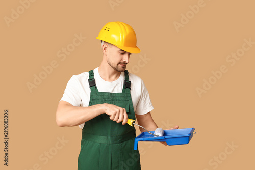 Portrait of male painter with tray and paint roller on beige background