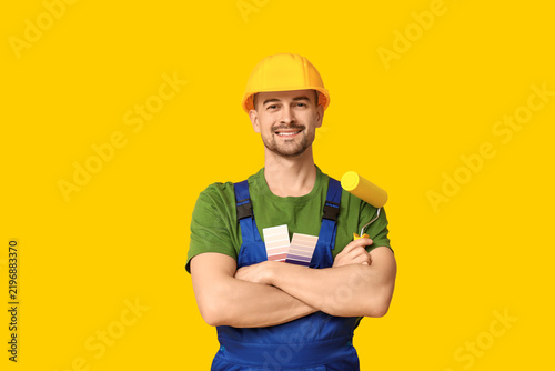 Portrait of male painter with color palettes and paint roller on yellow backg...