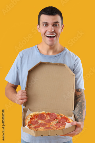 Young man with tasty pepperoni pizza on yellow background