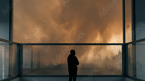 A lone figure stands silhouetted against a massive, swirling cloud formation viewed through a large window, evoking a sense of awe and trepidation at the power of nature.