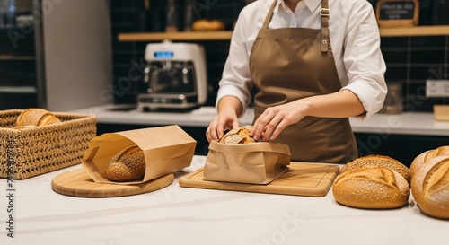 Baker carefully packaging freshly baked artisan bread loaves in brown paper bags on a wooden board at a counter