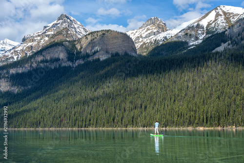 Man paddleboarding on Lake Louise with snow capped Rocky Mountains