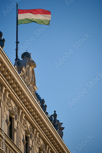 Fotografie Flag of Hungary flying above the ornamental roofline of a classic building again