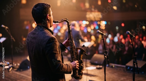 Saxophone player performing on stage at live concert event, jazz music performance atmosphere, musician entertainment industry concept, audience crowd background bokeh lights