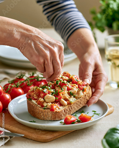 Woman preparing bean tomato toast at bright breakfast table