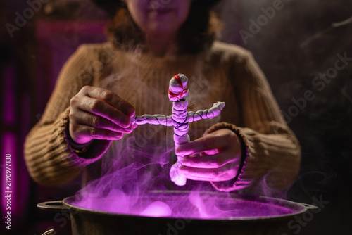 Foto realistic witch holding voodoo doll casts spell brewing potion in cauldron