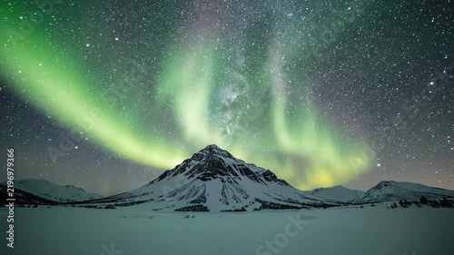 Vibrant green aurora borealis illuminates the night sky above a snow-covered mountain, surrounded by a starry backdrop.