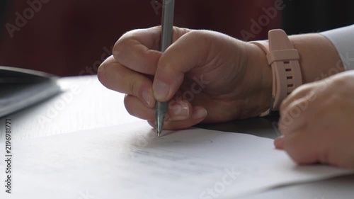 A close‑up of a woman’s hand signing with a pen. A woman’s hand writing on paper.