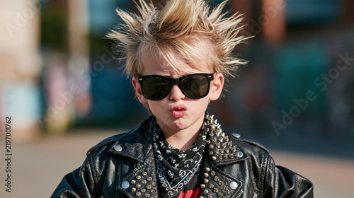 Young punk kid with spiky hair and leather jacket wearing sunglasses in urban portrait