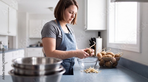 Young woman removes long sprouts from potatoes in her kitchen