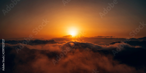 A sunrise over a mountain range with clouds and mist glowing in warm golden light. Dramatic sky and serene landscape, a peaceful and inspiring natural scene