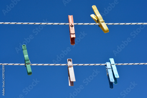 Fotografie Five vibrant plastic clothespins in various colors hang on two white washing lines against a clear blue sky background