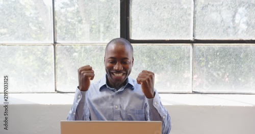 Businessman clapping hands and smiling while working on laptop by window