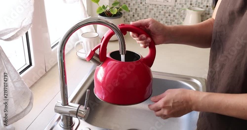 Pouring tap water into red kettle. Modern home resource utility trends. Daily kitchen household chore routine.
