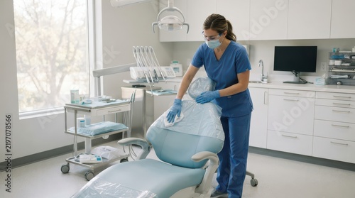 Masked dental worker wiping a chair covered with clear plastic