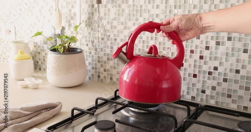 Placing red kettle on gas stove. Vintage home cooker kitchen appliances. Cozy morning routine cooking lifestyle.